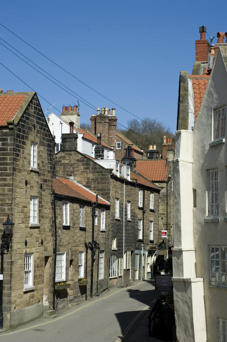 Narrow street in the fishing village of Robin Hoods Bay lined with traditional stone houses under a blue sunny sky