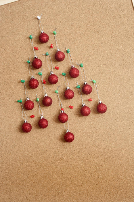 Office Christmas celebration with colorful red baubles formed into the shape of a Christmas tree on a cork noticeboard with copy-space - working Christmas