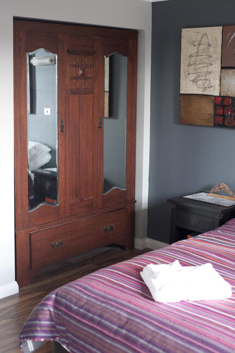Old wooden wardrobe with dual mirrors in bed and breakfast or hotel accommodation with fresh white towels laid out on a bed
