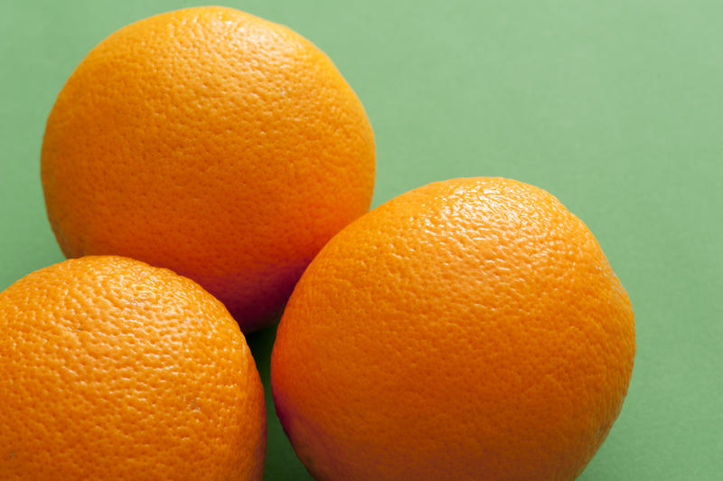 Three whole ripe oranges, natural source of vitamin C and antioxidants, high-angle close-up with copy space on green background