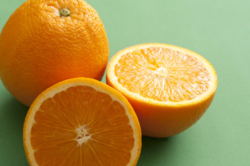 Whole and halved juicy fresh orange over a green background in a healthy diet and nutrition concept