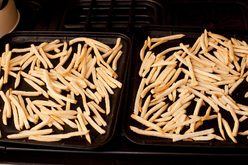 Oven baked French fries with the potato batons spread out to cook on a baking tray , high angle view