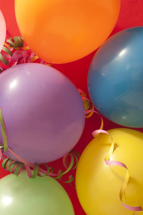 Close up Colored Birthday Party Balloons with Streamers Against Red Background
