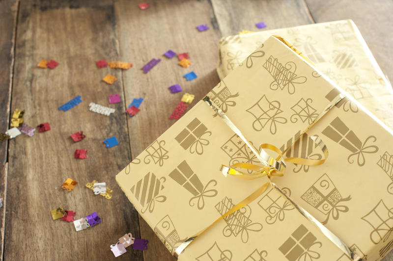 a gold coloured wrapped gift box with coloruful party scatters on a wood table