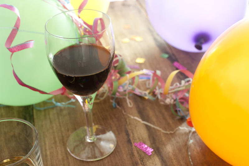 Party background of colorful balloons and streamers with a glass of red wine in the foreground on a wooden table