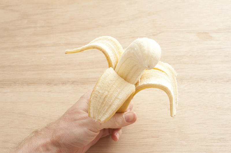 a hand holding a peeled half eaten banana with wood background