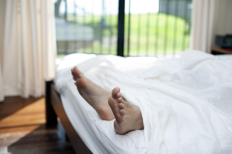 Man having a lazy day in bed with his feet protruding out from under the bedclothes with a close up view of his bare feet