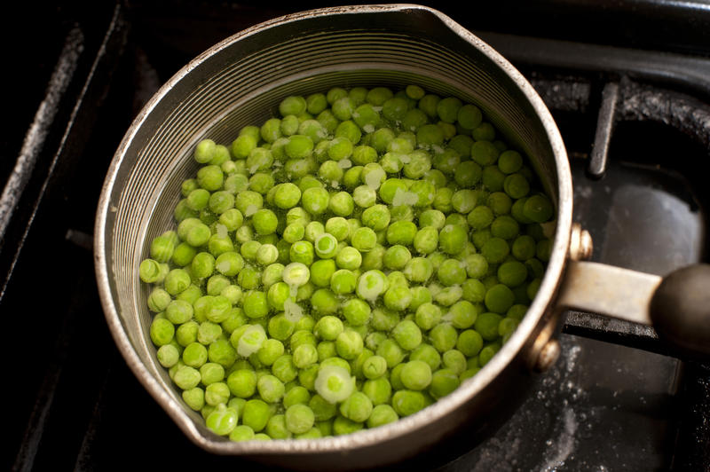 Fresh succulent young petit pois peas cooking in a saucepan on a gas hob, high angle view