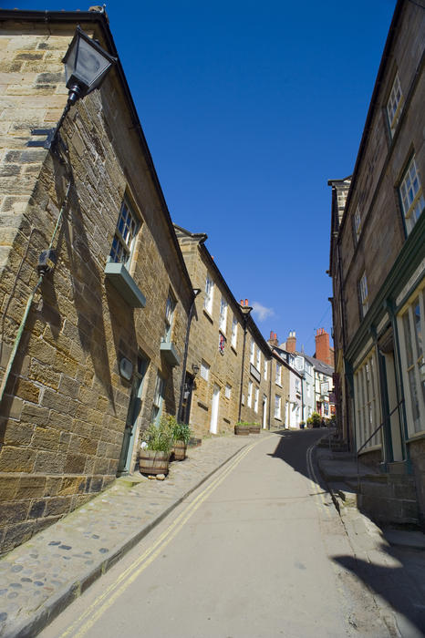 View up a deserted steeply curving Kings Street, Robin Hoods Bay, Yorkshire lined with traditional stone cottages