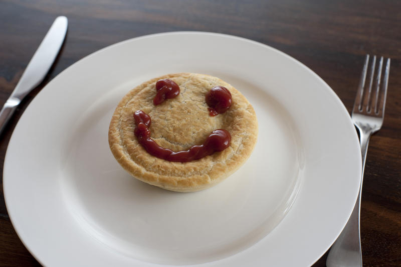 Meat pie with a smiley gravy face on the crusty pastry served on a plate for a lunchtime snack