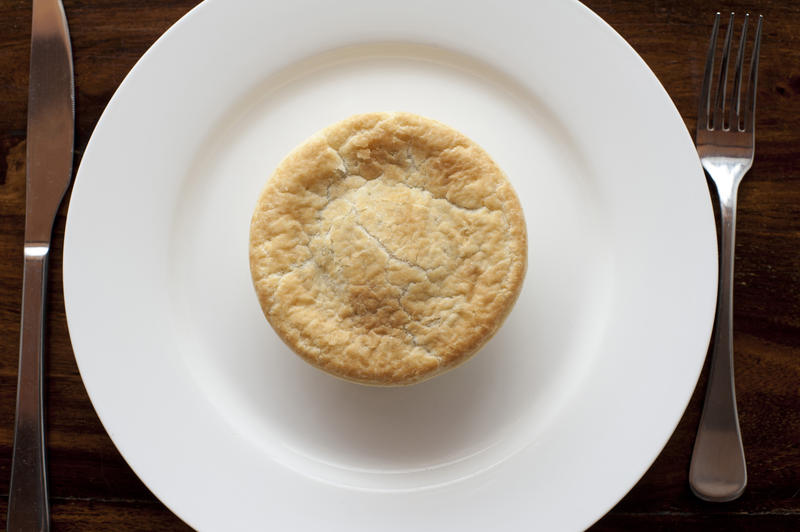 Freshly baked pastry meat pie with a flaky golden crust on a plain white plate viewed from above