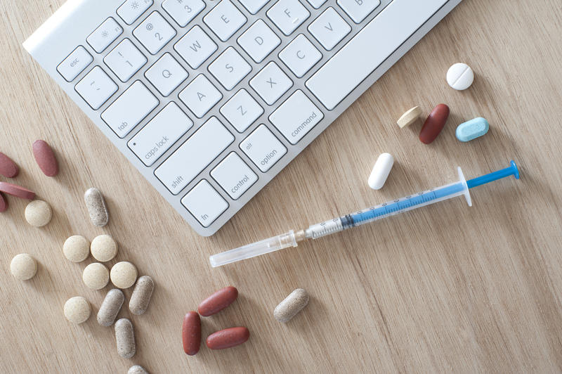 Online medicine and healthcare concept with an overhead view of a computer keyboard on a wooden desk with assorted pills and tablets and a disposable injection needle and syringe