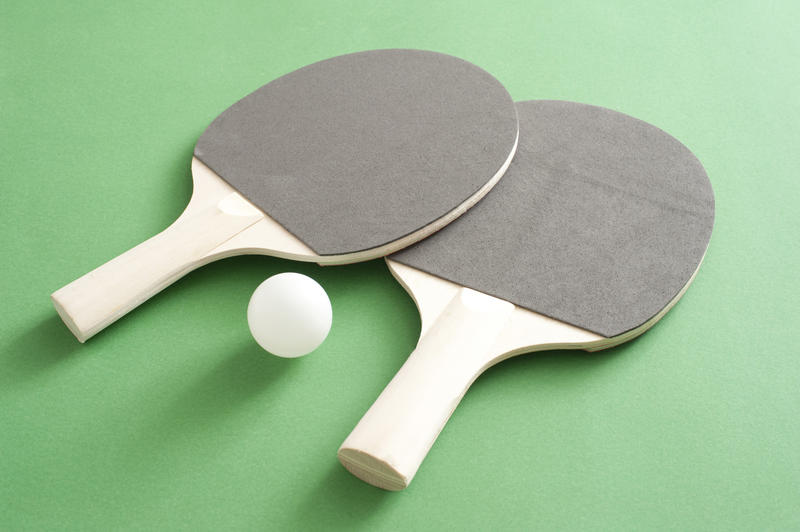 Two new table tennis bats and a ball lying on the green wooden table used to play the game