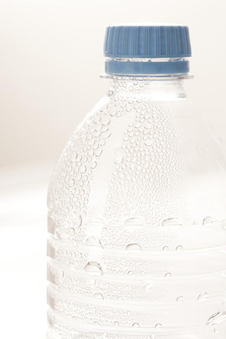 Chilled fresh mineral water in a plastic bottle with beaded condensation on the outside and a blue cap, closeup on white