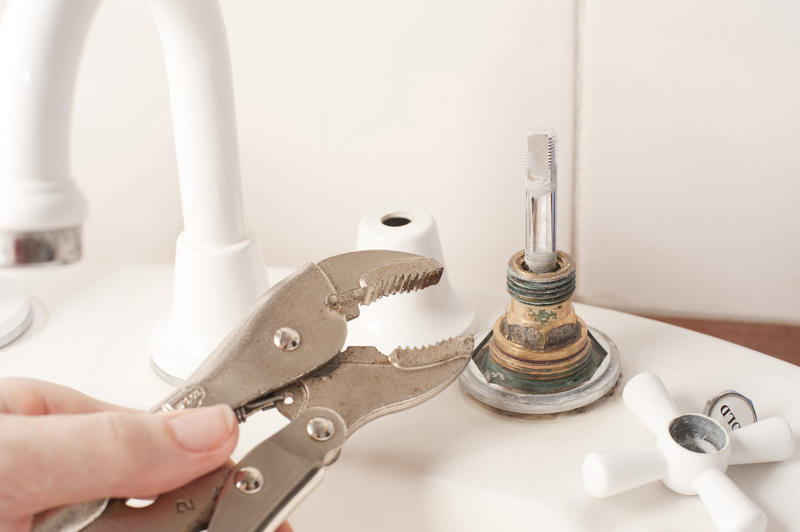 Man repairing a faucet or tap in the bathroom with a mole grip pliers during house renovations