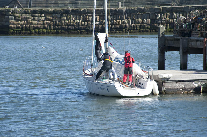 j92 Sailing yacht moored alongside a jetty in Whitby harbour with the crew getting ready to take it out for a sail and removing the covers on the sails