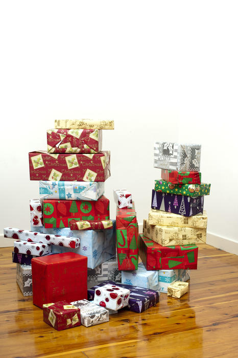 Stack of colourful Xmas presents and packages in traditional patterned seasonal gift wrap paper on a hardwood floor with a white wall background with copyspace