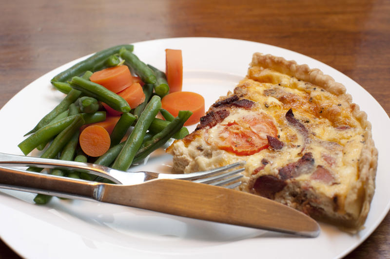 Slice of savoury quiche with a crispy crust served with cooked fresh green beans and carrots for a healthy light meal or snack