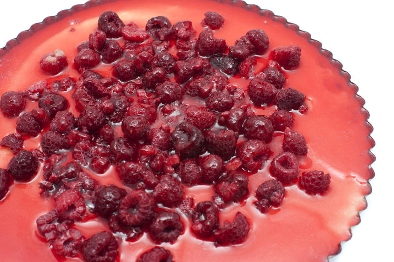 Delicious freshly baked whole ricotta cheesecake with raspberries in a fluted pie pan, high angle close up view over white