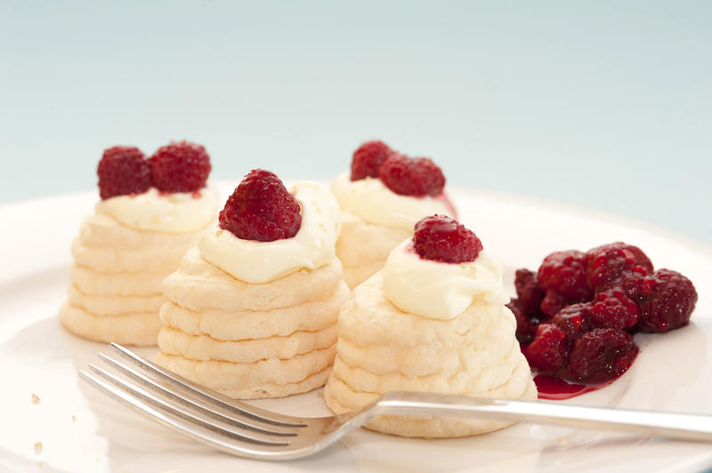 Serving on a plate of mini meringue pavlovas with decorative twirled cases filled with whipped cream and raspberries