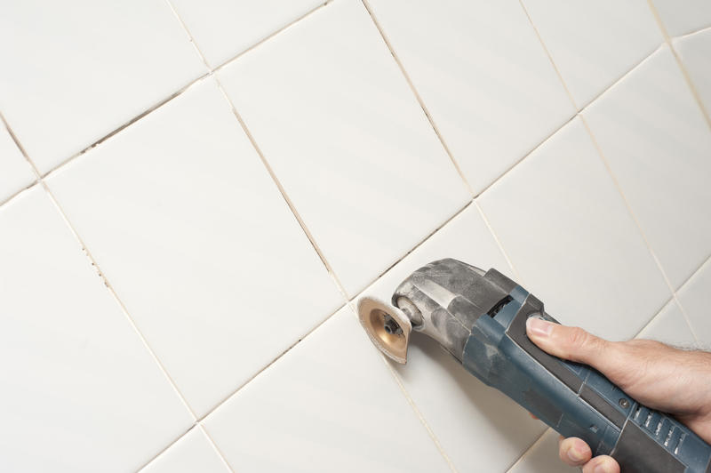 Man removing grout between wall tiles using a handheld oscillating tool in a DIY, renovation and redecorating concept