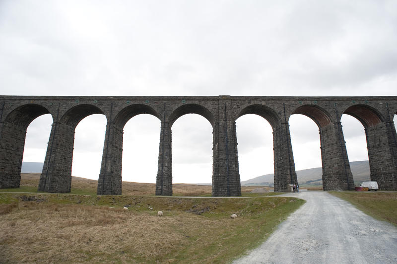 Low angle view of the stone arches of the Ribblehead Railway viaduct as it crosses the valley and the River Ribble with a road in the foreground