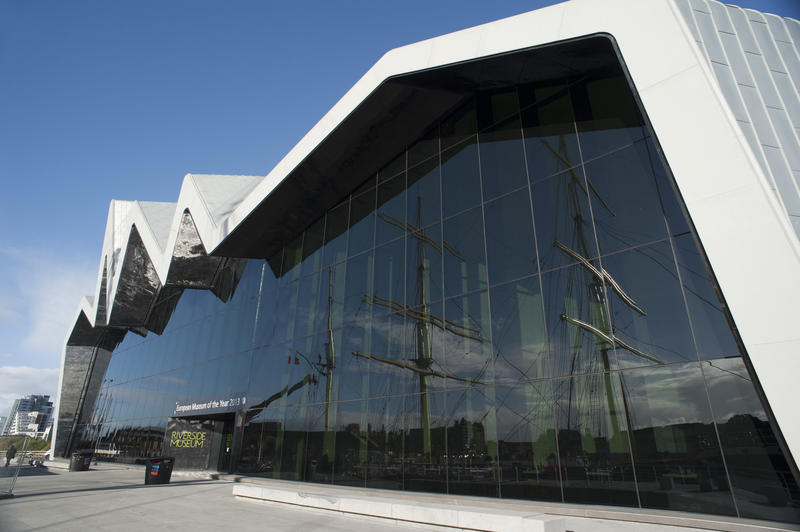 Exterior facade of the Glasgow Riverside Museum with its modern zigzag design and large window reflecting tall ships on the riverside