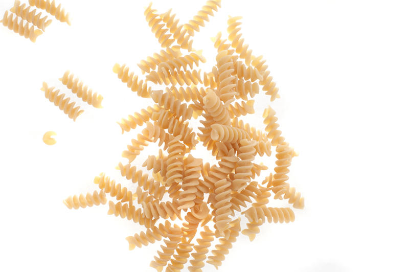 Dried rotini Italian pasta scattered on a white surface showing the twisted spiral form of the noodles, overhead view