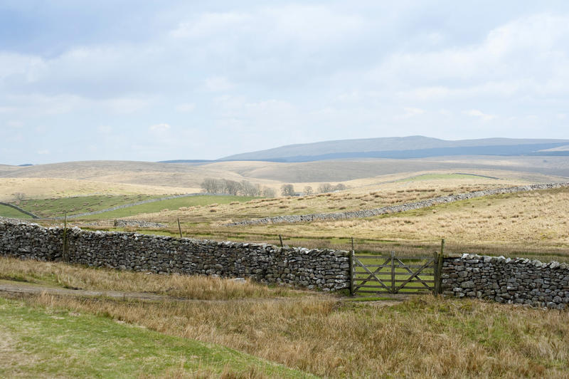 Rural English landscape with rolling gentle hills and a farm gate set in a dry-stone wall in the foreground