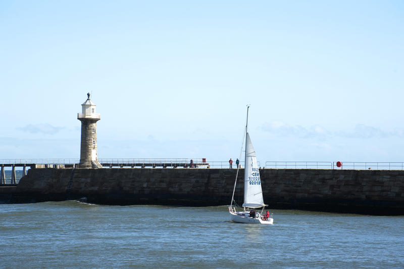 j92 Yacht sailing past the Whitby breakwaters and pier at the entrance to the harbour as it heads for the open sea
