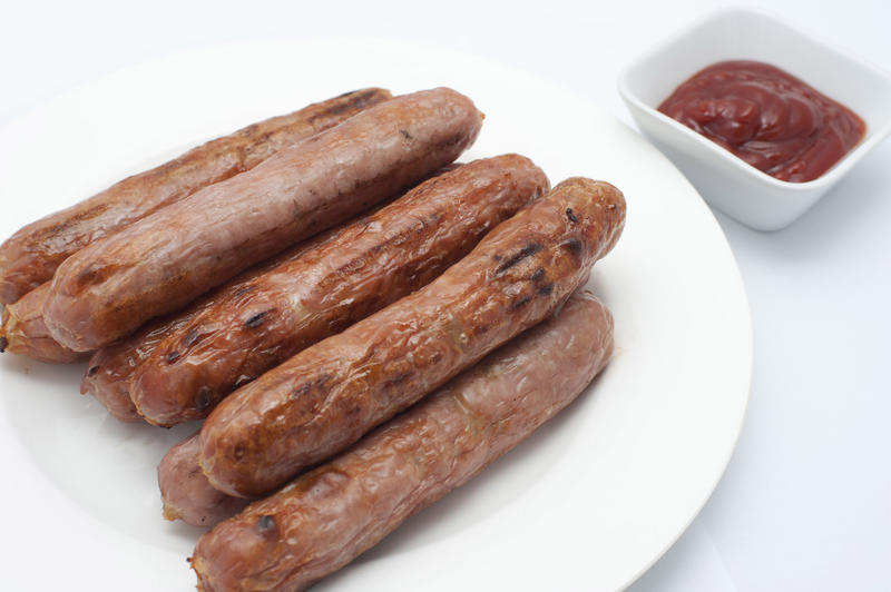 Pile of grilled spicy sausages on a plate with a side serving of tomato ketchup in a dish for dipping