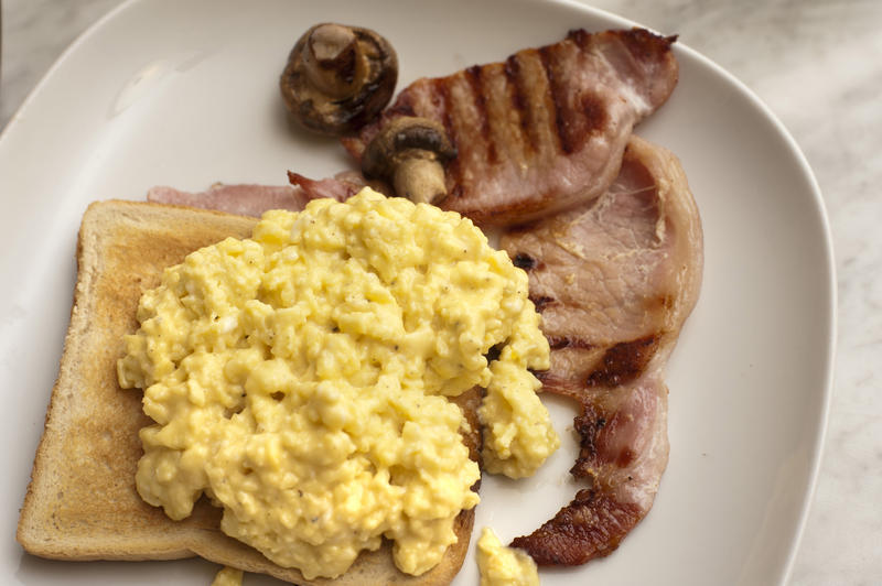 Scrambled eggs for breakfast served on toast with rashers of grilled bacon and mushrooms