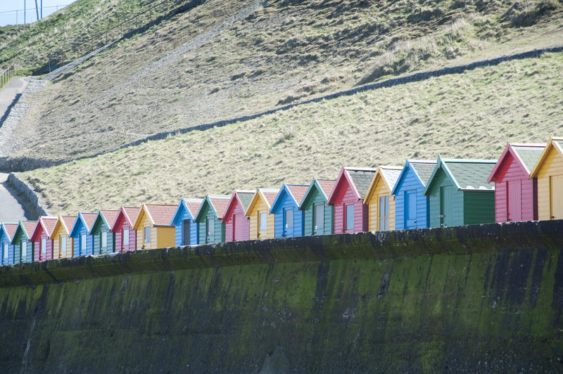 Row of brightly painted wooden beach huts on Whitby West Cliff and Whitby sands