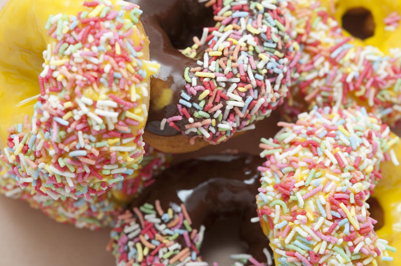 Selection of ring donuts with chocolate, orange and lemon glaze covered in colorful candy sprinkles for a coffee break or party, close up view