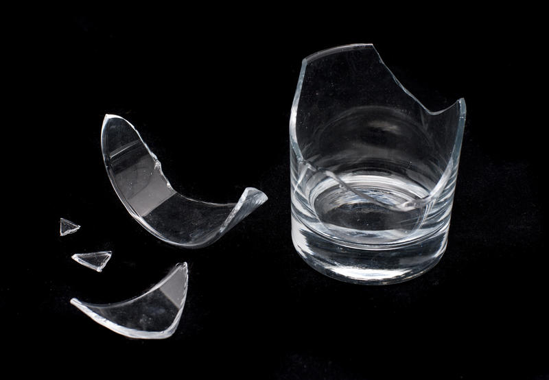 Remnants of a broken glass on a black background with the remains of the tumbler and loose shards with jagged edges