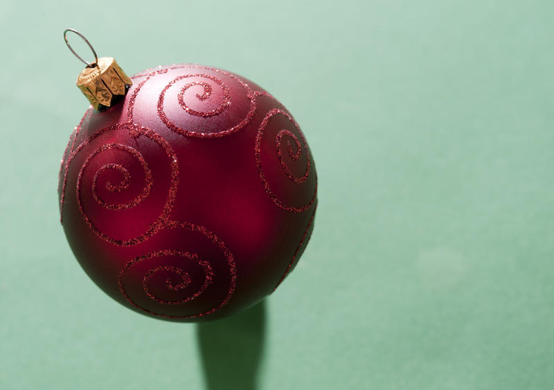 Textured red Christmas bauble on a green background with copyspace to the right for your seasonal greeting