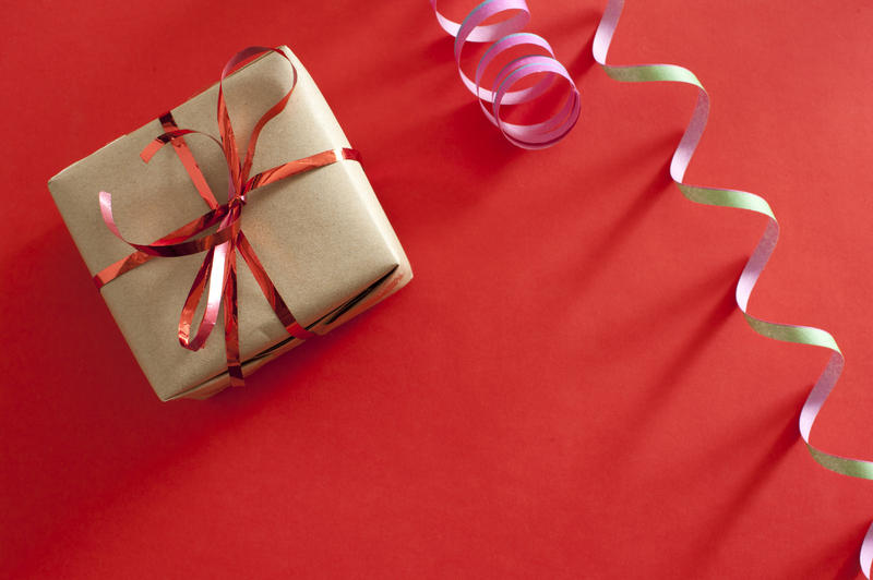 Festive background with a small gift tied with a red bow and party streamer over a red background with copyspace for your greeting, view from above