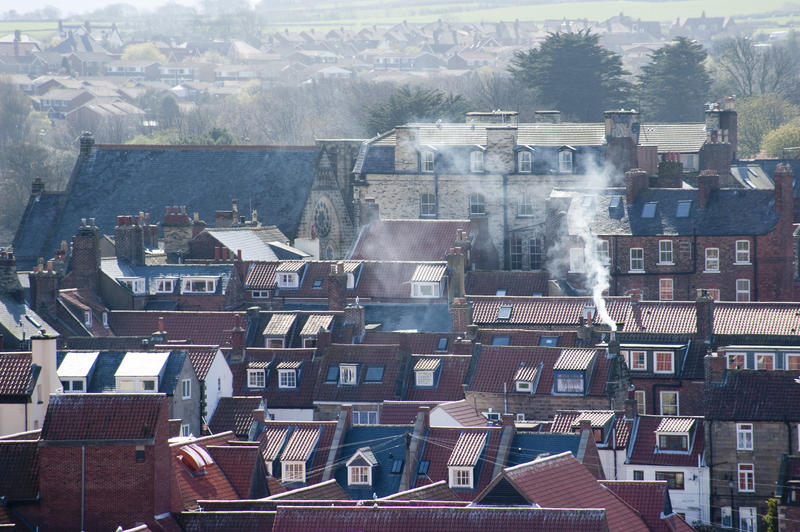 View over rooftops and smoking chimneys from the fires in cottages below in the coastal town of Whitby in Yorkshire, England