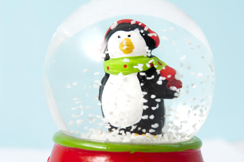 Cute little penguin in a shaken snow globe with swirling winter snowflakes engulfing him as though in a snowstorm, a symbolic Christmas ornament