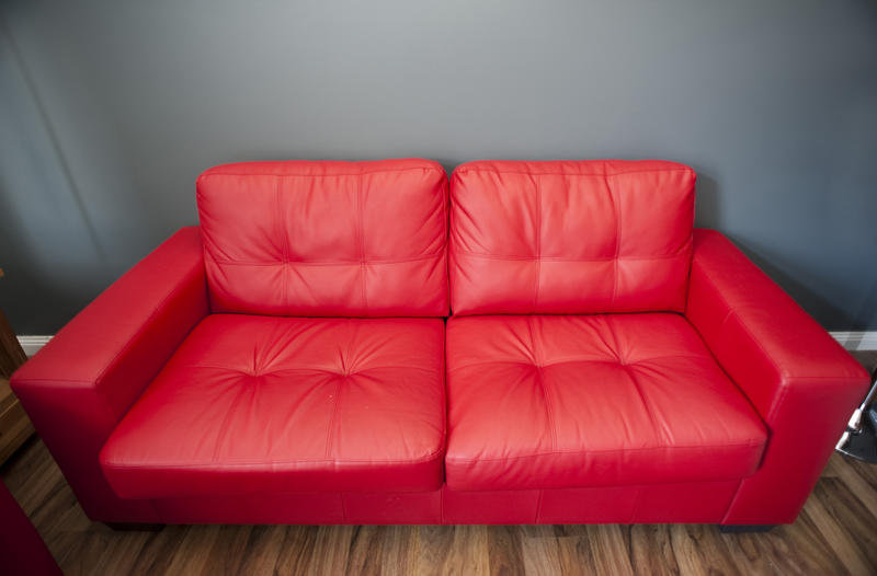 Close up high angle view of a generic comfortable red upholstered leather sofa on a wooden parquet floor in an interior decor concept