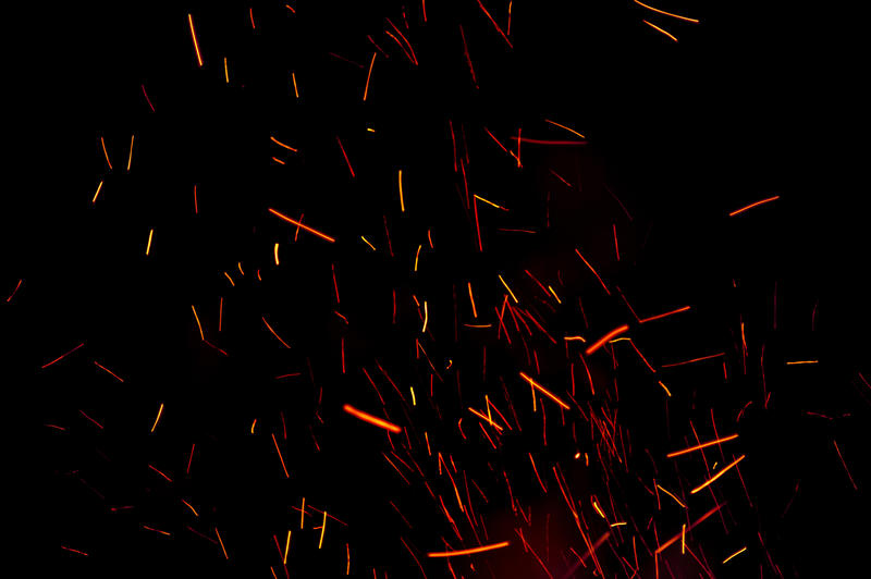 Background of fiery burning embers leaving an abstract pattern of motion colorful orange trails in the darkness above a bonfire or campfire
