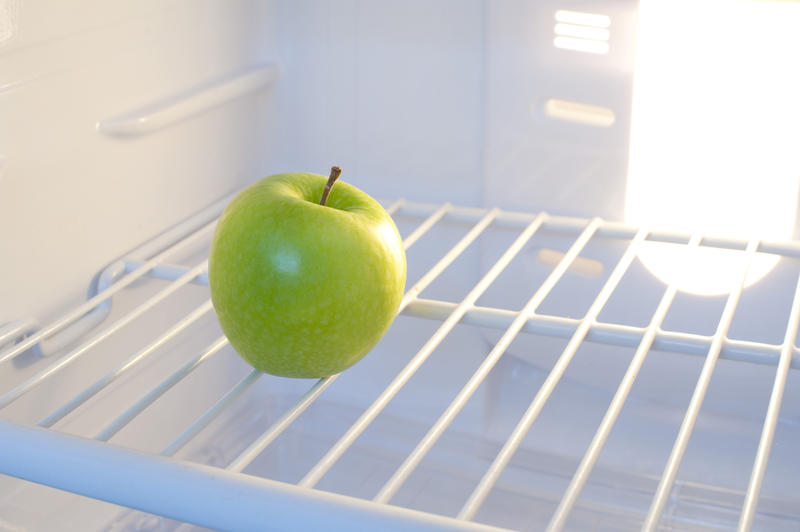 Single delicious healthy green apple inside a domestic fridge with wire shelving backlit by the interior electric light