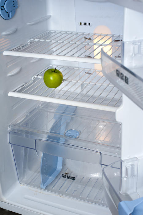 a bare shelves of a fridge with no food inside but a single green apple