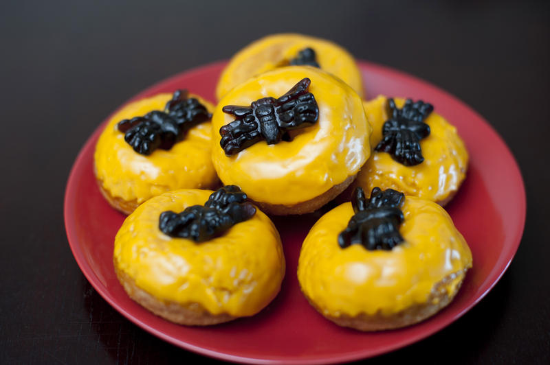 Plate of colourful orange frosted Halloween doughnuts topped with scary black jelly spiders for celebrating the festival or as a tasty cake for young trick-or-treating kids