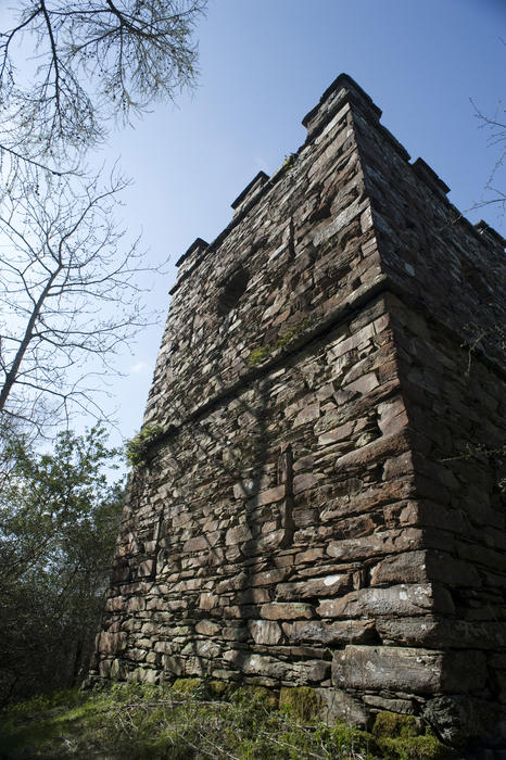 Old historical stone folly built in the form of a crenallated tower with ramparts viewed from below