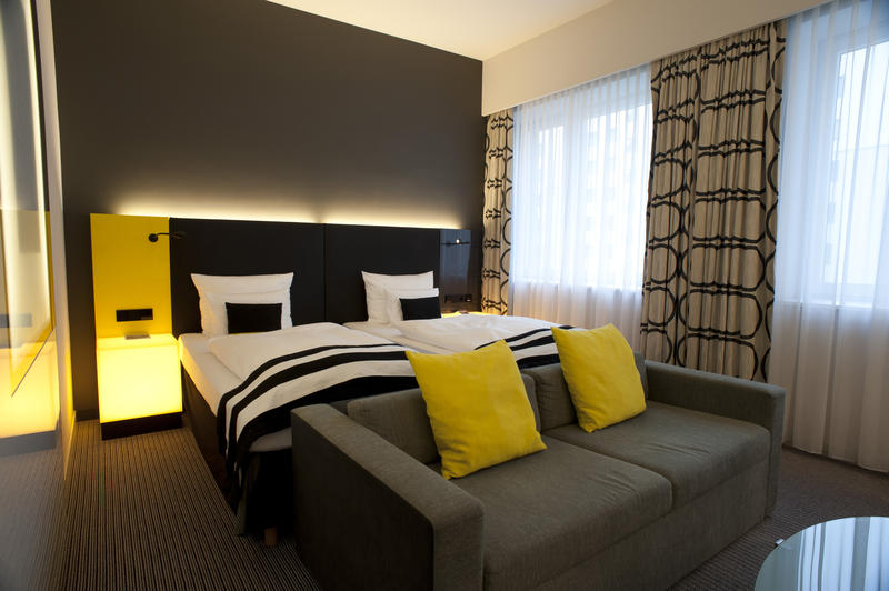 Stylish modern bedroom with a king size bed, comfortable sofa and table with yellow cushions and matching accents in an interior decor and accommodation concept