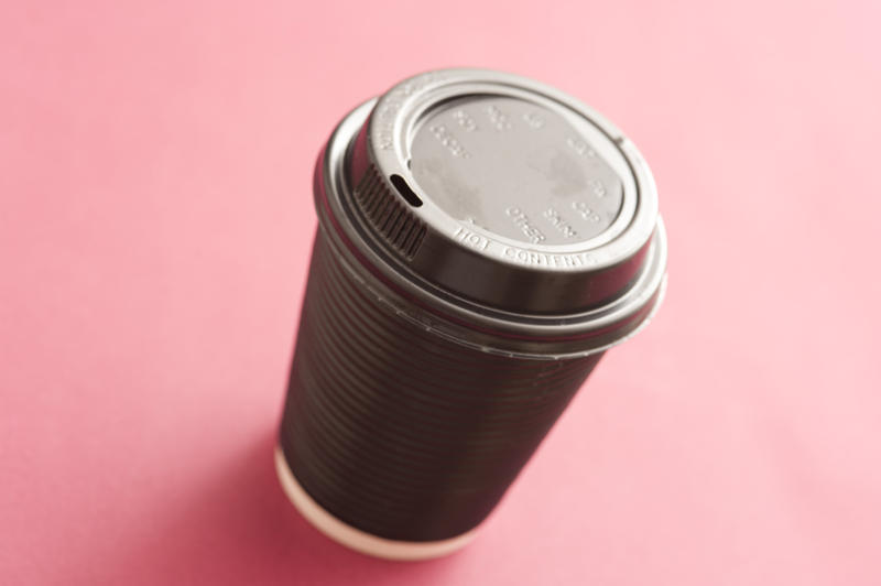 Takeaway coffee from a cafeteria in a disposable plastic cup with a closed lid, high angle on pink