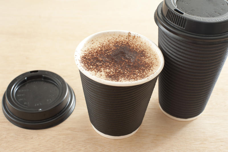 Takeaway cappuccino coffee in two disposable cups, one open to show the frothy coffee inside, high angle view
