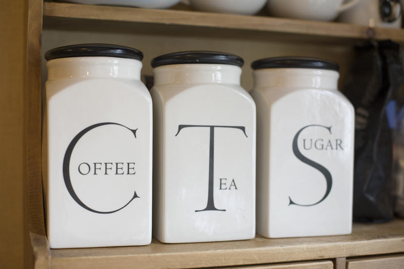 Set of labelled ceramic jars for tea, sugar and coffee standing in a row on the shelf of a wooden kitchen dresser, close up angled view