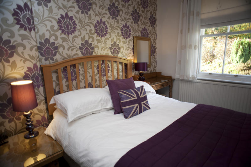 Themed British bedroom with a comfortable wooden double bedstead with decorative wallpaper and cushions bearing the Union Jack